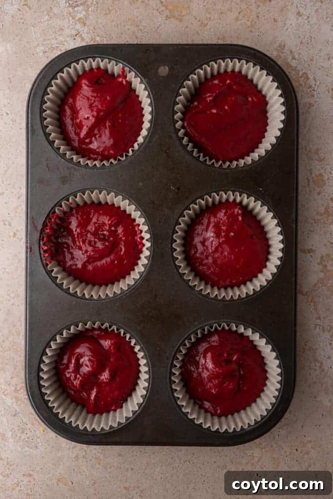 A muffin pan filled with raw red velvet cupcake batter, ready for baking.