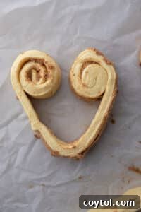 Cinnamon roll dough strip partially rolled from each side, forming the top curves of a heart.