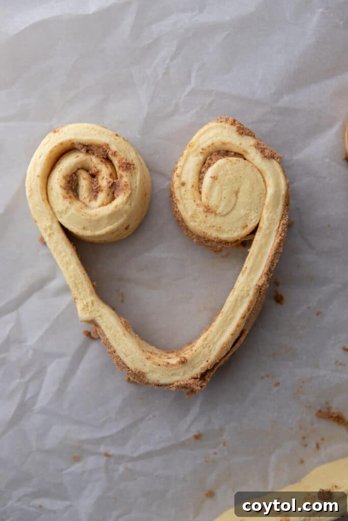 A single unbaked cinnamon roll dough strip, meticulously shaped into a perfect heart, resting on a sheet of parchment paper, ready for baking.