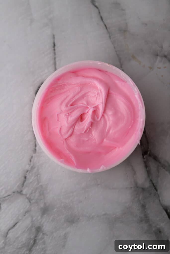 A small bowl filled with vibrant pink icing, perfectly mixed and ready to be drizzled or spread over warm cinnamon rolls, hinting at the festive final touch.