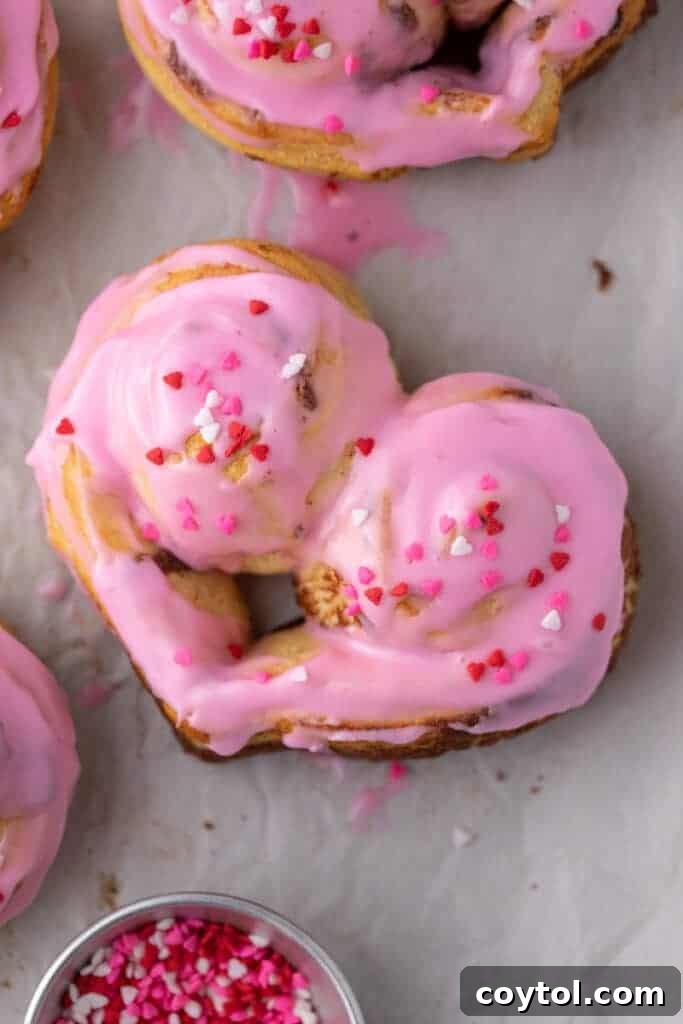 A delectable spread of frosted heart-shaped cinnamon rolls, featuring a beautiful pink icing and a generous topping of Valentine’s sprinkles, arranged invitingly on a platter.