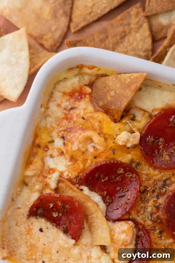 A close-up view of the cottage cheese pizza bowl dip in a dish, with a chip submerged.