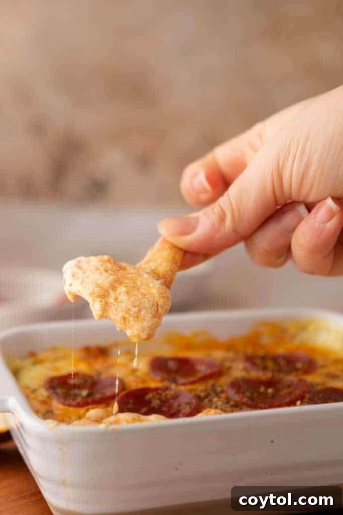 A hand holding a chip with a scoop of cottage cheese pizza bowl dip.