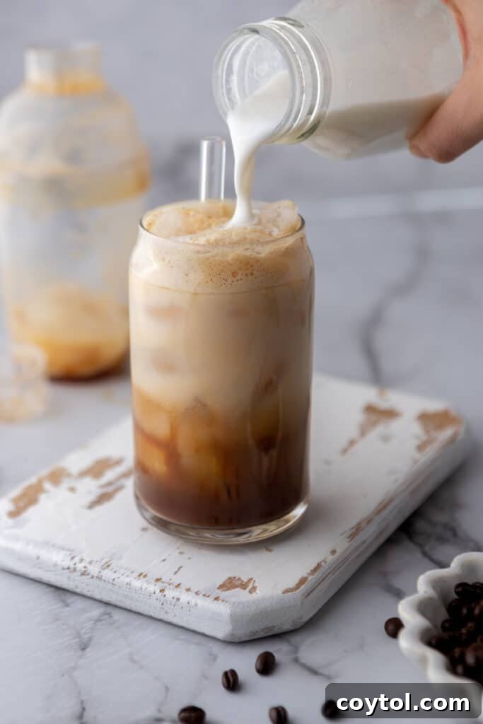 Creamy oat milk is gently poured over the frothy, shaken espresso and ice in a tall glass, completing the Iced Hazelnut Oatmilk Shaken Espresso.