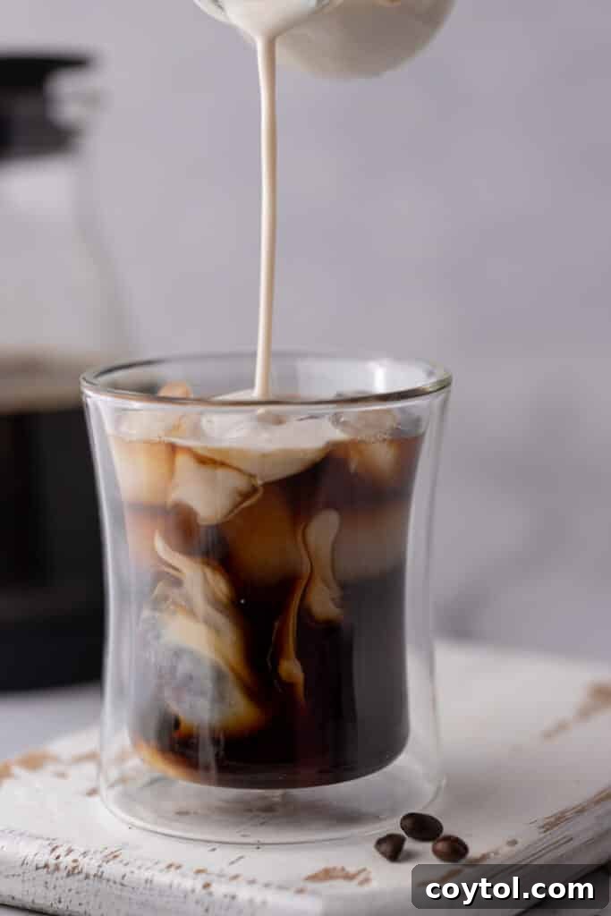 Person pouring cold brew concentrate into a glass of iced coffee