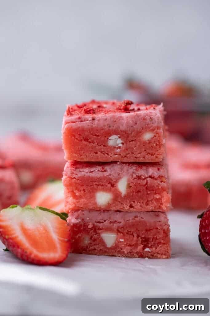 Three decadent strawberry brownies, perfectly stacked, showcasing their vibrant pink hue and tempting glaze.