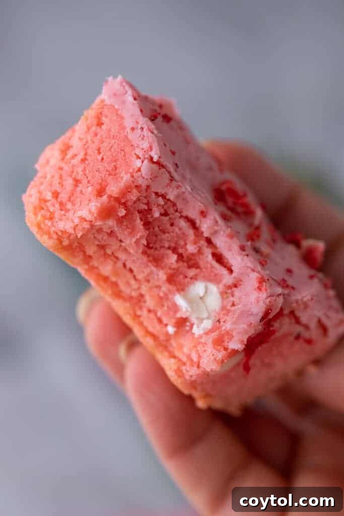 Close-up of a delightful strawberry brownie with a corner bitten off, showcasing its fudgy texture and pink glaze.