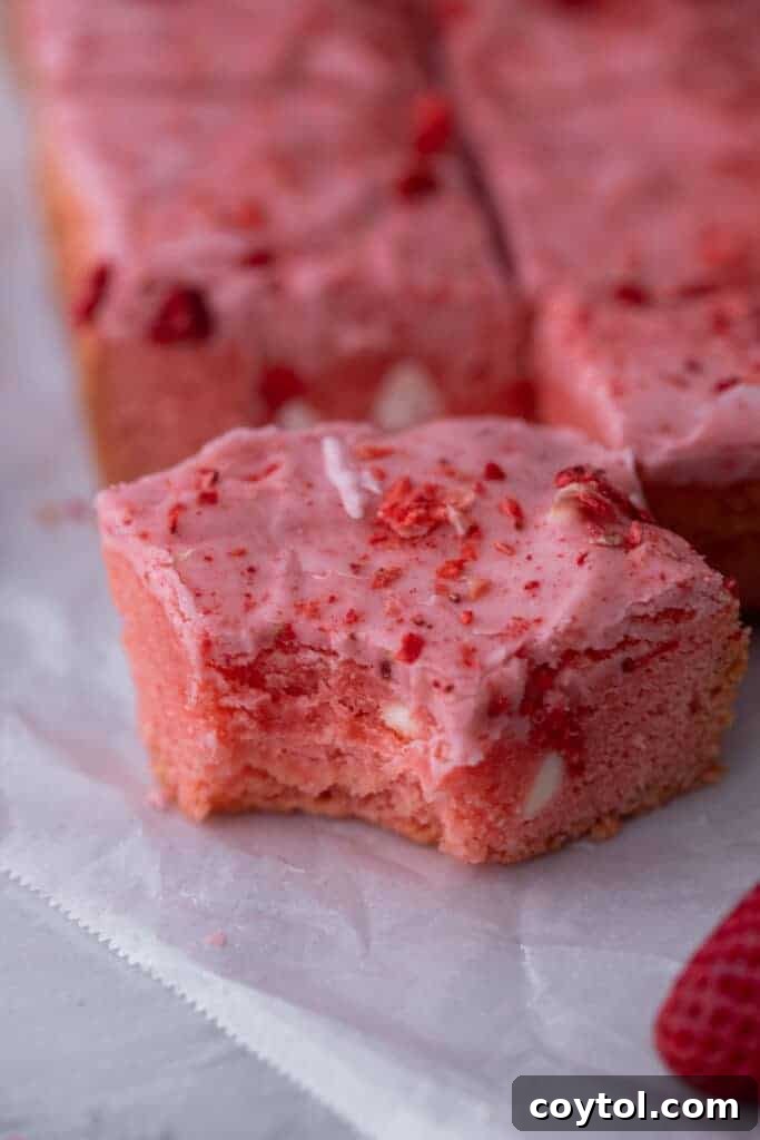 Close-up shot of a single strawberry brownie with a bite taken out, revealing its rich, fudgy interior and pink glaze.