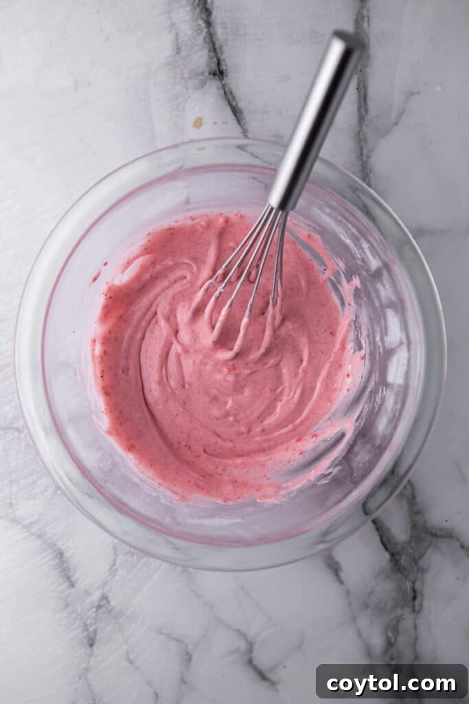Strawberry glaze being whisked to perfection in a bowl, showing its creamy, pink consistency.