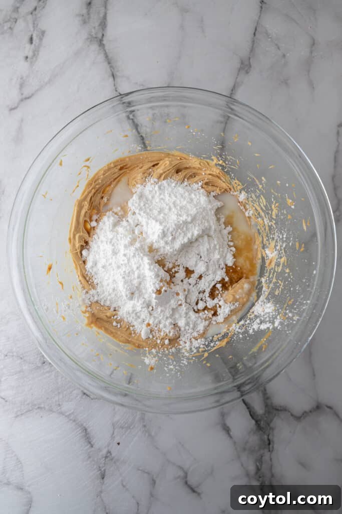 Powdered sugar being added over the creamed peanut butter and butter mixture in a mixing bowl.