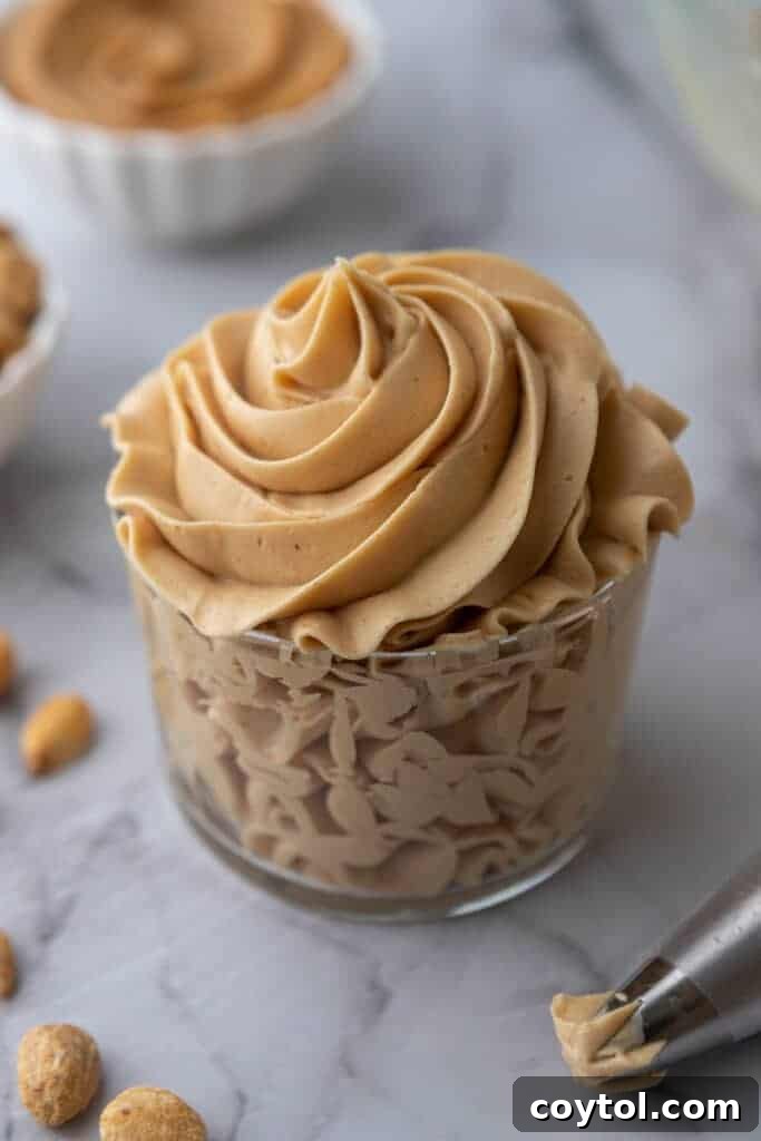 Angled overhead shot of smooth peanut butter frosting in a small glass cup, ready to be served.