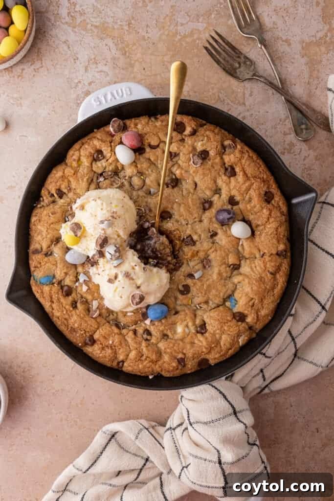 A large, golden brown Cadbury Mini Egg Skillet Cookie, baked in a cast iron pan and ready to be served, showcasing its vibrant candy pieces.