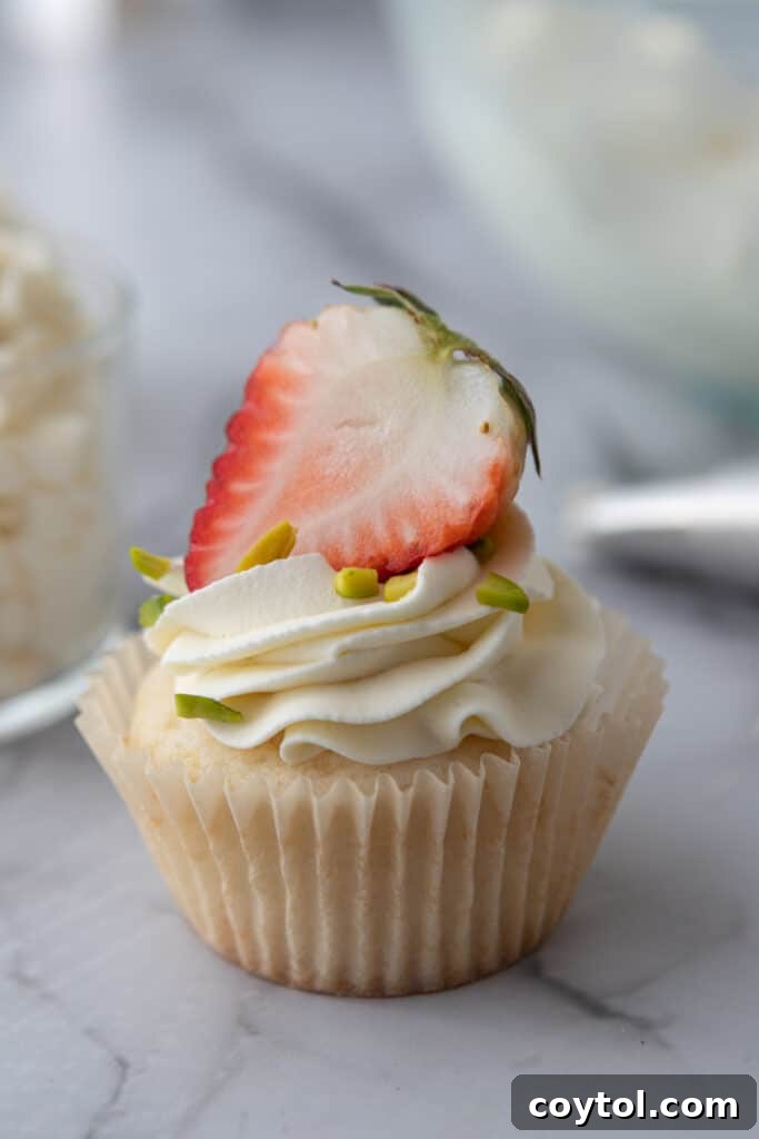 A cupcake topped with creamy mascarpone frosting and a fresh strawberry, ready to be enjoyed.