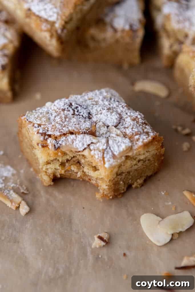 A square of almond croissant blondies with a bite taken out of it, showcasing its chewy texture and almond topping.