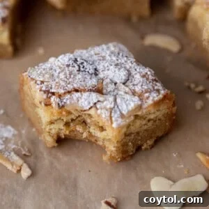 A square of almond croissant blondies with a bite taken out of it, showing the chewy texture and frangipane swirl.