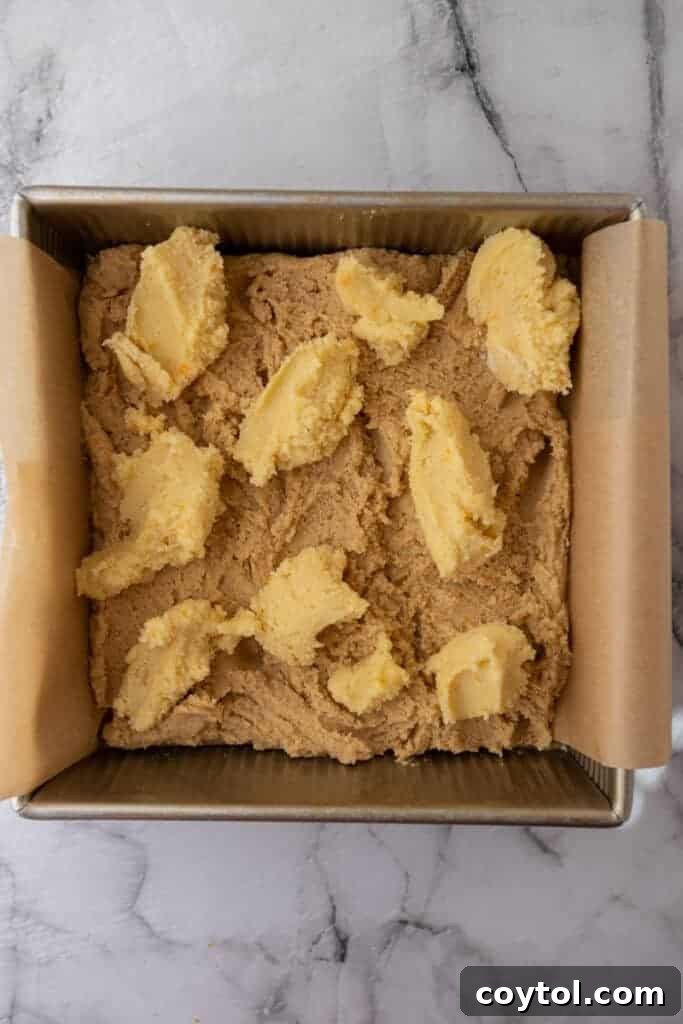 Almond frangipane dolloped over blondie batter in a baking pan.