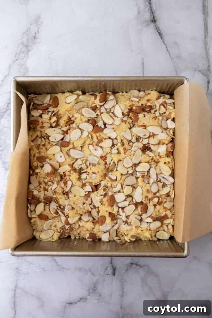 Raw almond croissant blondies in a pan, topped with sliced almonds, before baking.