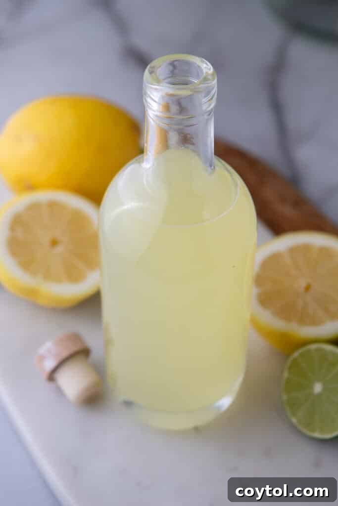 Easy Homemade Lemon Sour Mix Recipe 7 Overhead shot of a bottle of homemade lemon sour mix on a marble surface, surrounded by lemons and limes.