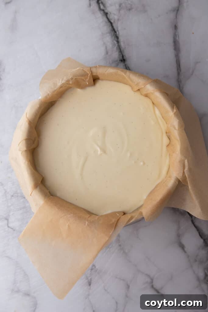 Raw Basque cheesecake batter poured into a parchment-lined springform pan, ready for the oven.