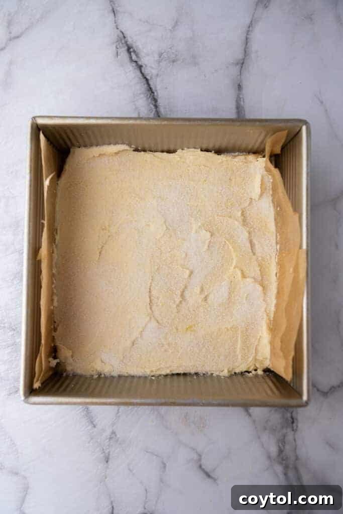 Lemon cookie dough spread evenly in a parchment-lined baking pan, ready for the oven