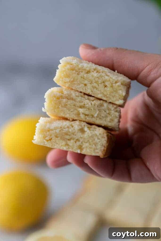 A hand reaching for a piece of freshly baked lemon sugar cookie bar from a tray
