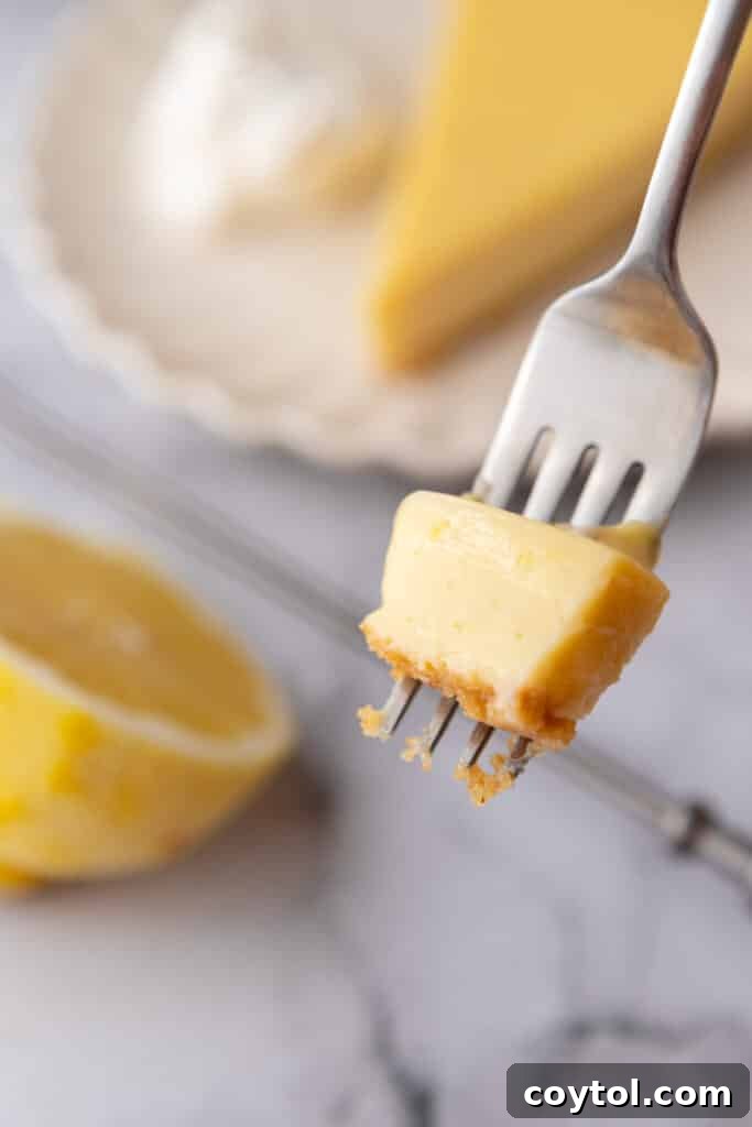 A close-up shot of a fork taking a bite from a slice of lemon pie, showing the creamy filling and crunchy crust.