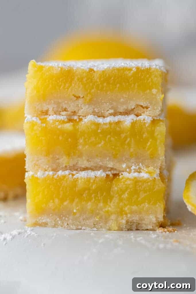 Three golden-yellow lemon bars stacked delicately, showcasing their powdery sugar dusting and thick, zesty filling over a shortbread crust.