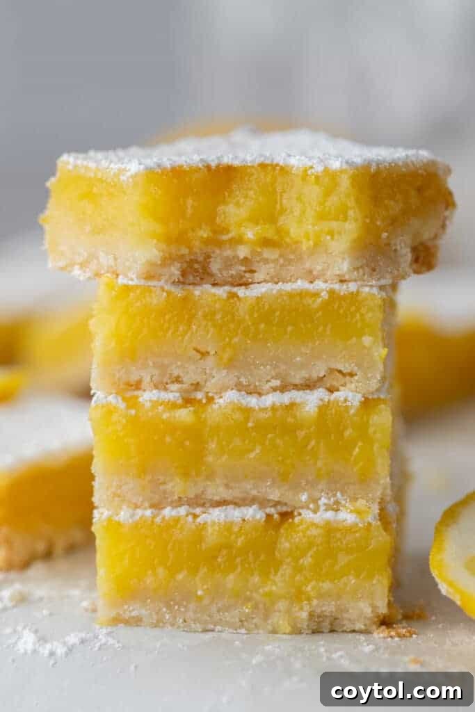 Four perfectly cut lemon bar squares, generously dusted with powdered sugar, stacked neatly on a plate.