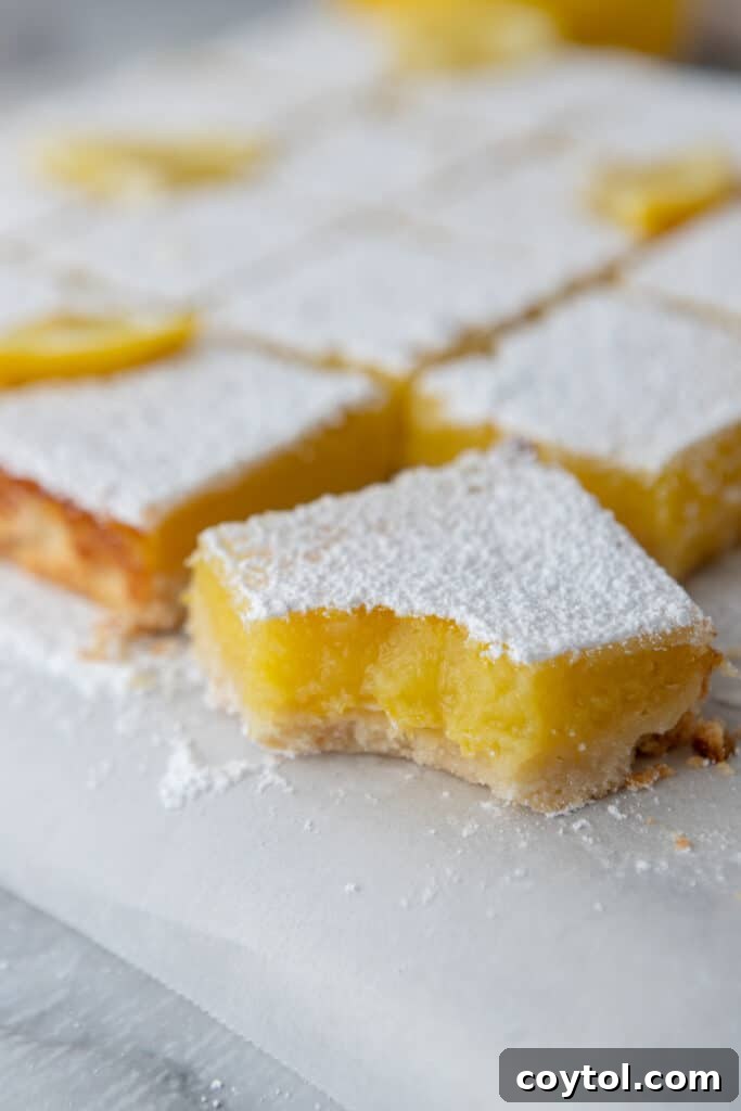 A freshly cut lemon bar square with a bite taken out, showing the vibrant yellow filling and the crumbly shortbread crust.