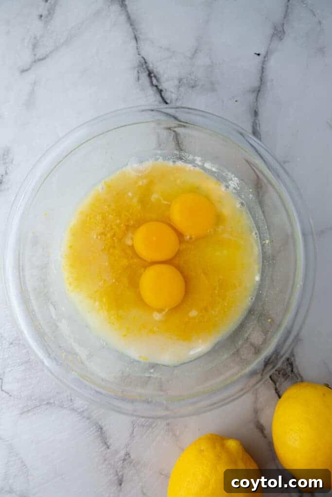 Fresh eggs, lemon juice, zest, and sugar for the lemon bar filling in a bowl.