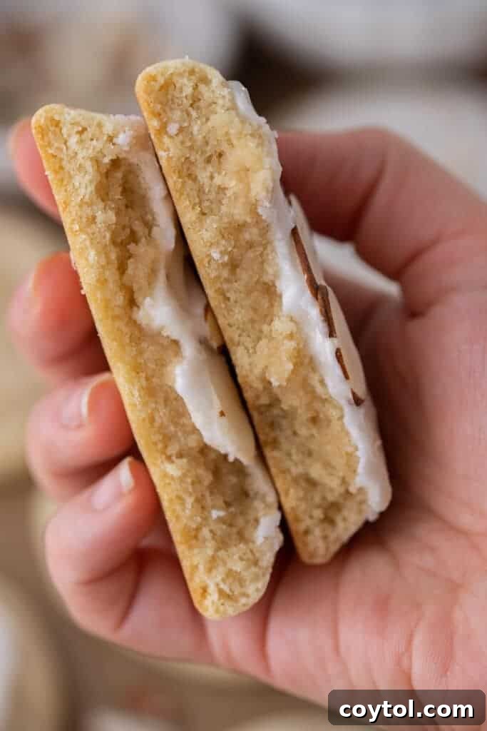 A hand presenting a stack of soft, iced almond sugar cookies