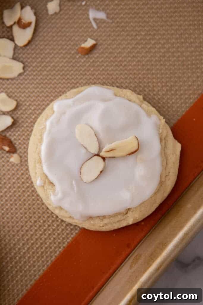 A freshly frosted soft almond sugar cookie adorned with sliced almonds on a baking sheet
