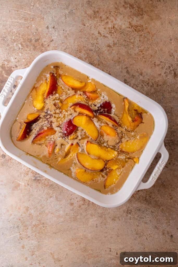 Cobbler batter poured over melted butter, topped with peaches in a baking dish, before baking