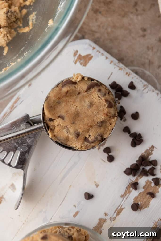 Irresistible Edible Chocolate Chip Cookie Dough 4 A perfectly portioned scoop of glistening, edible chocolate chip cookie dough sits invitingly on a wooden board, showcasing its rich texture and plentiful chocolate chips.