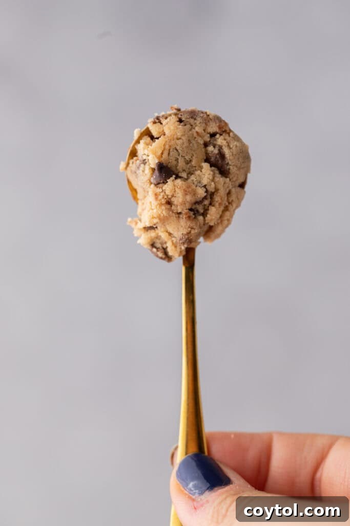 Irresistible Edible Chocolate Chip Cookie Dough 10 A close-up shot of a spoon scooping a generous portion of edible chocolate chip cookie dough, highlighting its delightful texture and visible chocolate pieces.