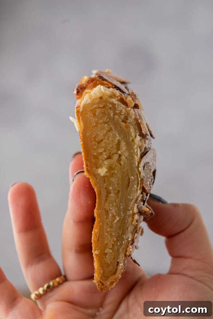 A hand holding up a piece of the golden-brown Braided Almond Croissant Danish, showcasing its flaky layers.