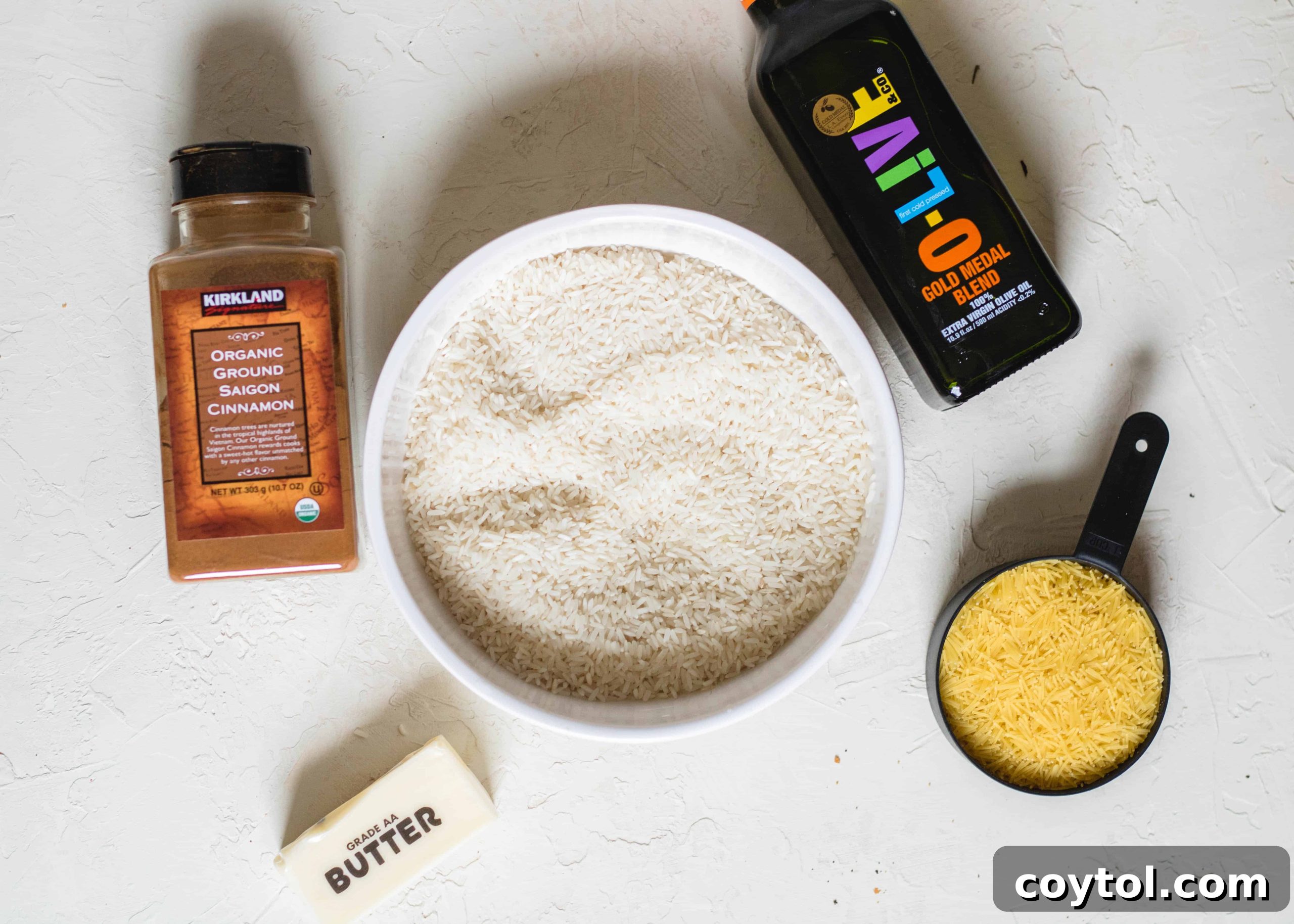 A selection of essential ingredients for making stovetop rice pilaf: long-grain white rice, vermicelli noodles, butter, and cinnamon, arranged on a rustic wooden surface.