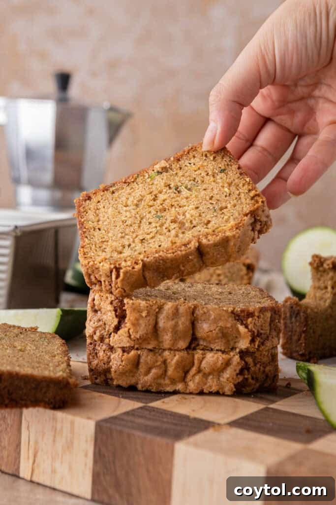 A hand picking up a slice of golden-brown zucchini bread, showcasing its moist texture and delicious crumb.