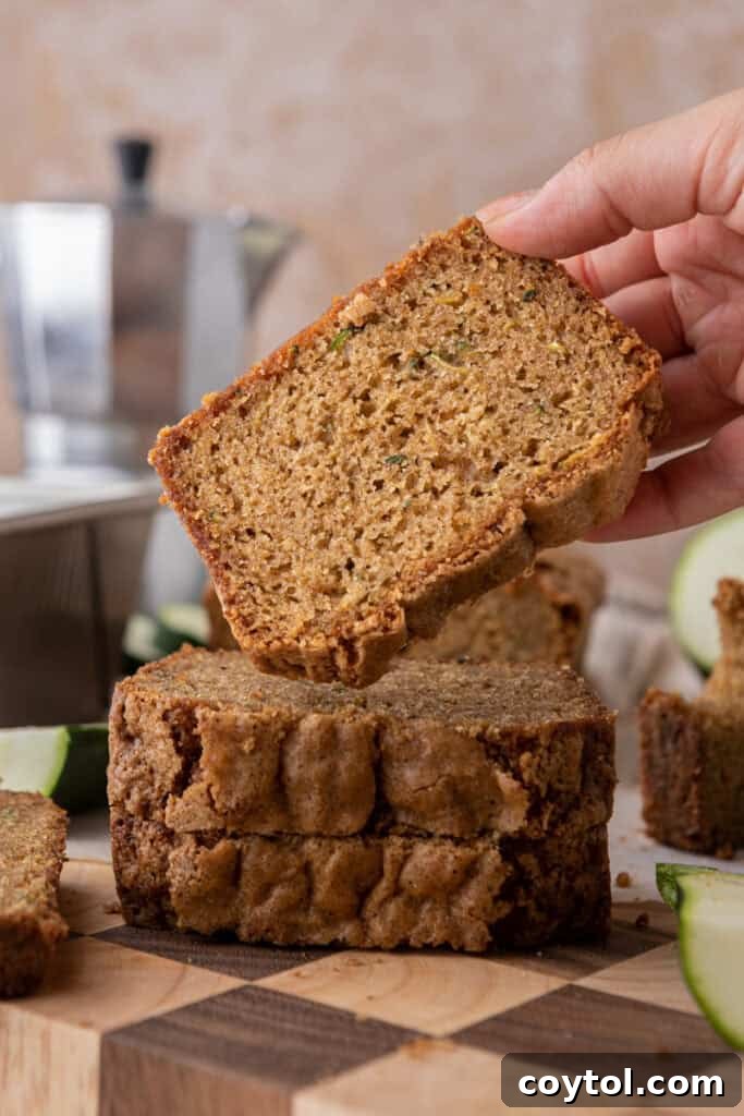 A hand reaching for a slice of freshly baked zucchini bread, highlighting its appeal.