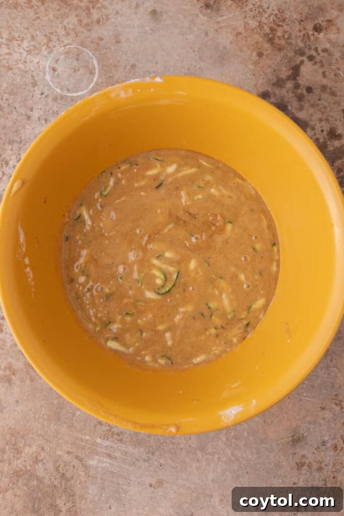 Grated zucchini mixed into the wet ingredients, showing even distribution.
