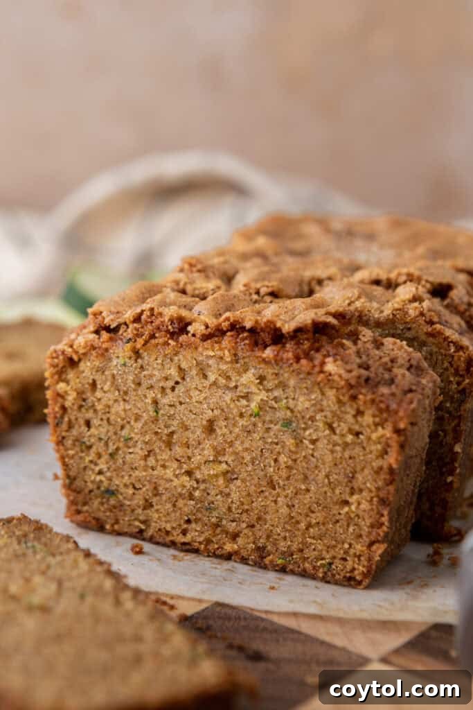 A side shot of a beautifully baked zucchini bread loaf on a cooling rack, showcasing its height and golden crust.