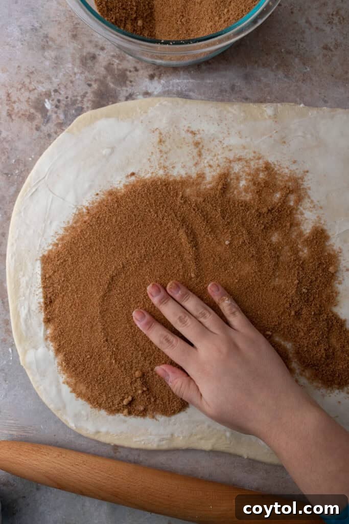 Cinnamon sugar filling generously spread over the buttered, rolled-out dough, ready for rolling.