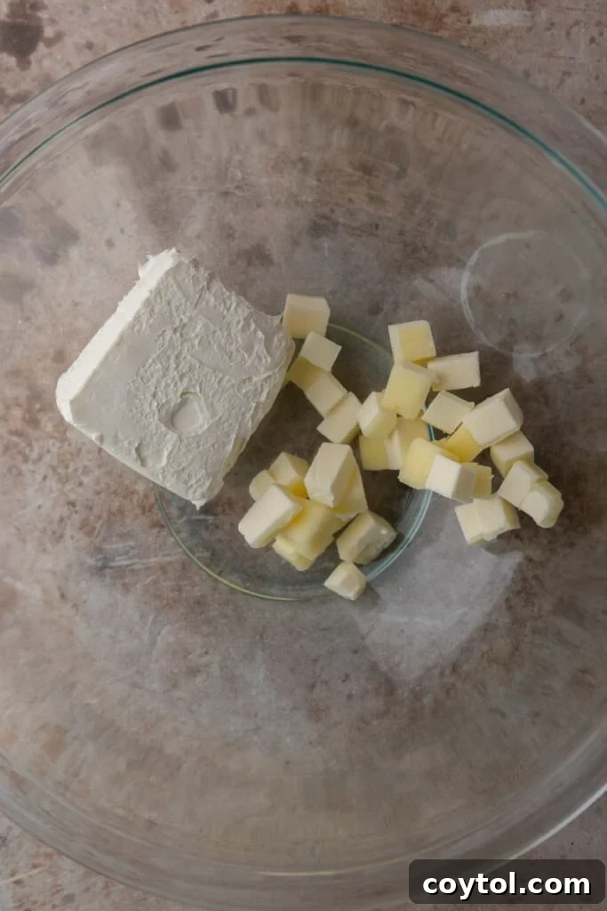 Unmixed cream cheese, butter, and powdered sugar, the key ingredients for frosting, in a bowl.