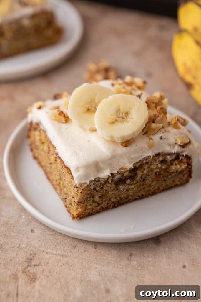 A perfectly sliced piece of moist banana cake with cream cheese frosting on a white plate, ready to be enjoyed.
