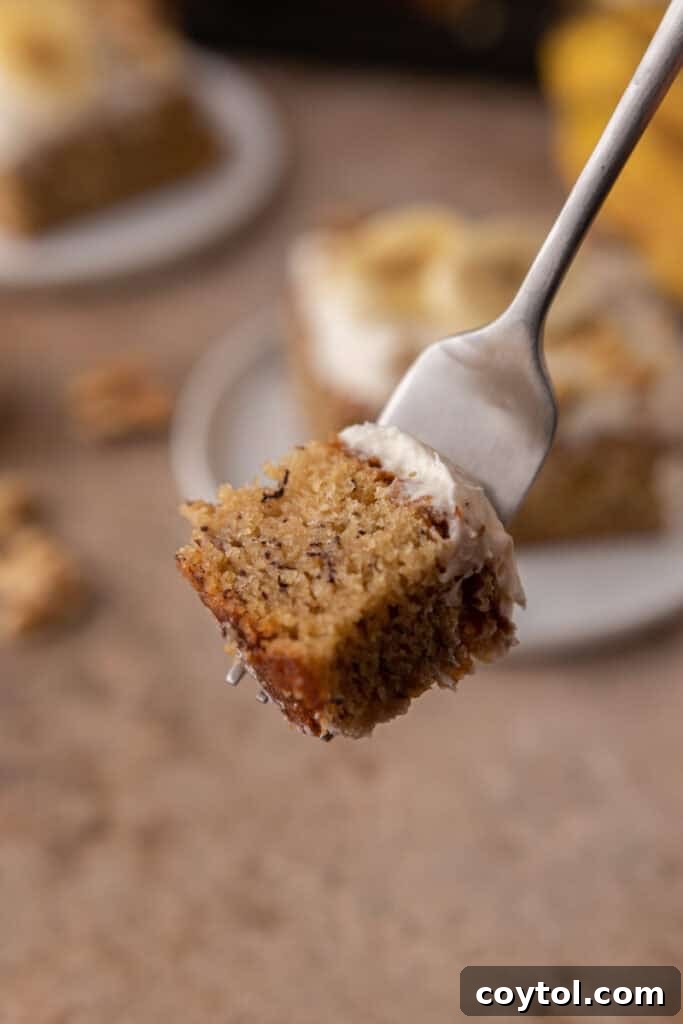 A close-up shot of a fork with a small bite of banana cake, showing the moist crumb and creamy frosting.