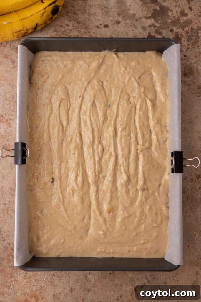 Unbaked banana cake batter poured into a prepared 9x13 inch baking pan, ready for the oven.