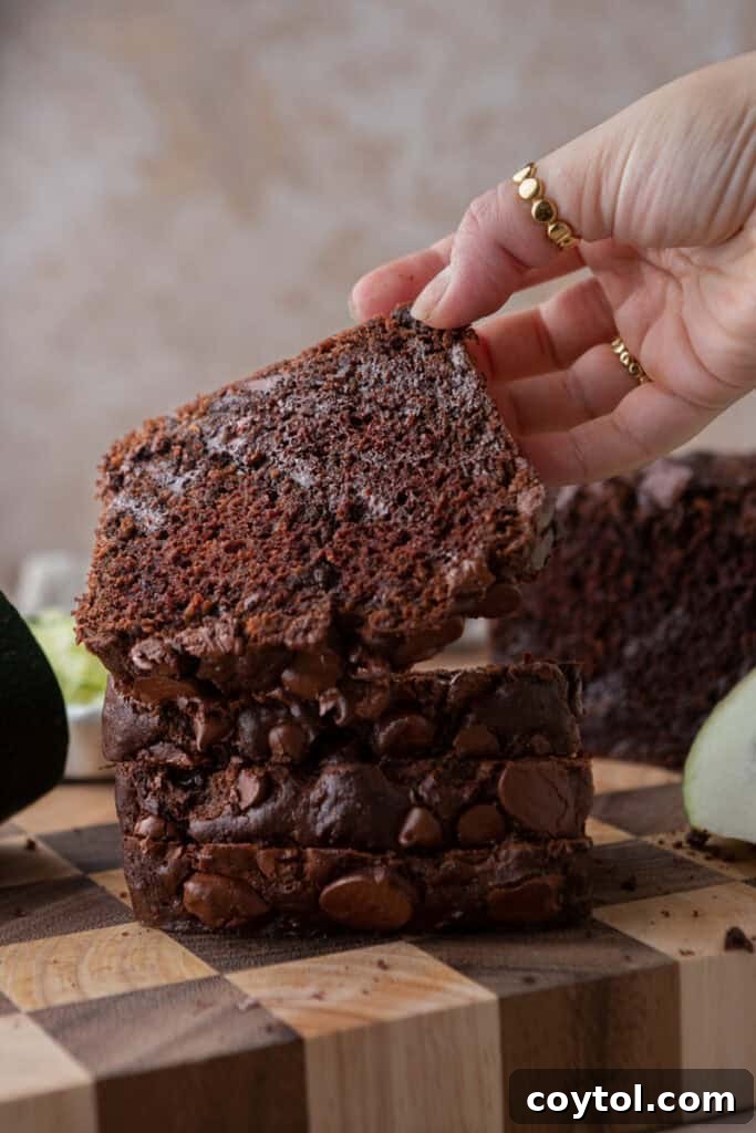 Side shot of the Double Chocolate Zucchini Bread recipe being picked up by a hand, ready to be eaten.