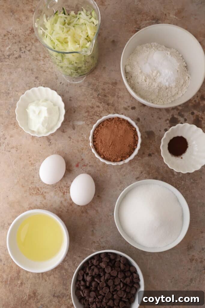 Ingredients for Double Chocolate Zucchini Bread laid out on a counter, including flour, cocoa powder, eggs, oil, sugar, vanilla, shredded zucchini, and chocolate chips.