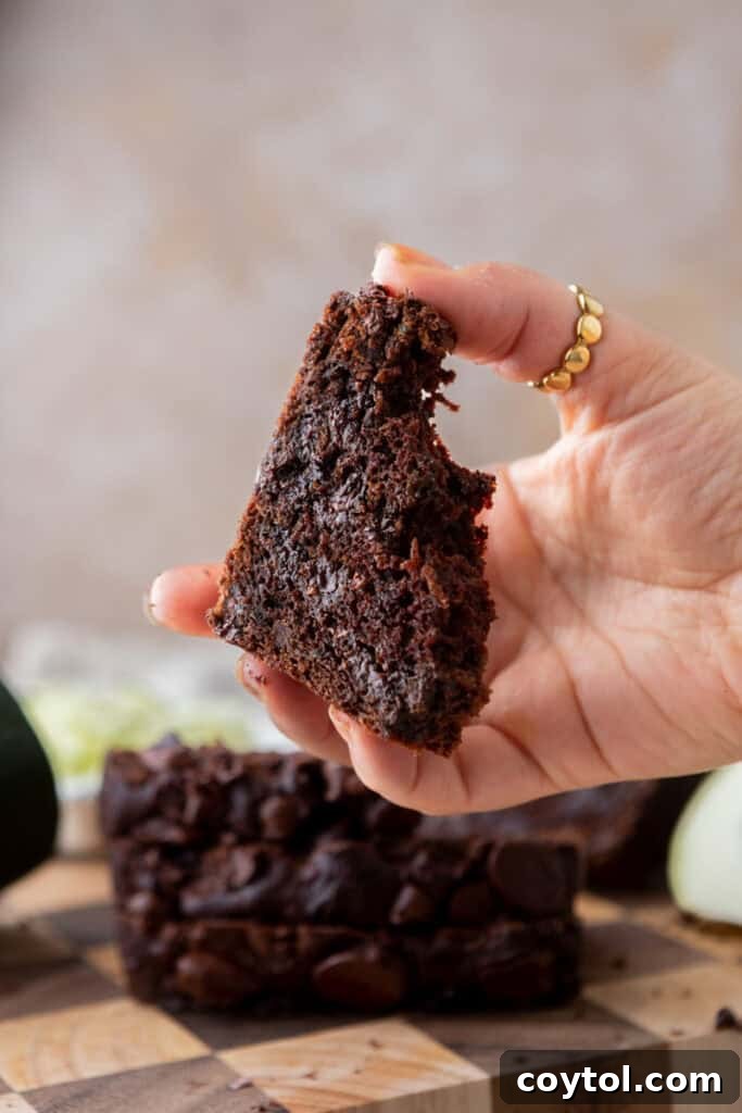 A hand holding a slice of Double Chocolate Zucchini Bread, showing its rich, dark color and moist texture.