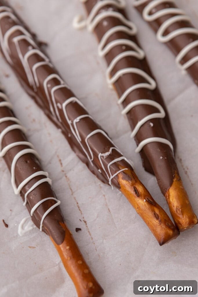 A close-up shot of three caramel chocolate covered pretzel rods arranged neatly on a sheet pan, showcasing their different toppings and perfect coatings.